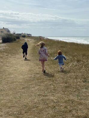 A pathway leading to the sea with grass and a few buildings in the background.