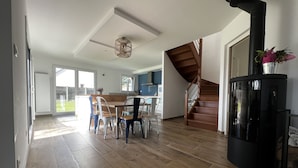 A spacious living area with a wooden floor, a dining table with chairs, a staircase, and a black stove. - La Villa Case-bi, Profitez en Famille de ce Magnifique Logement (Saint-Germain-sur-Ay)