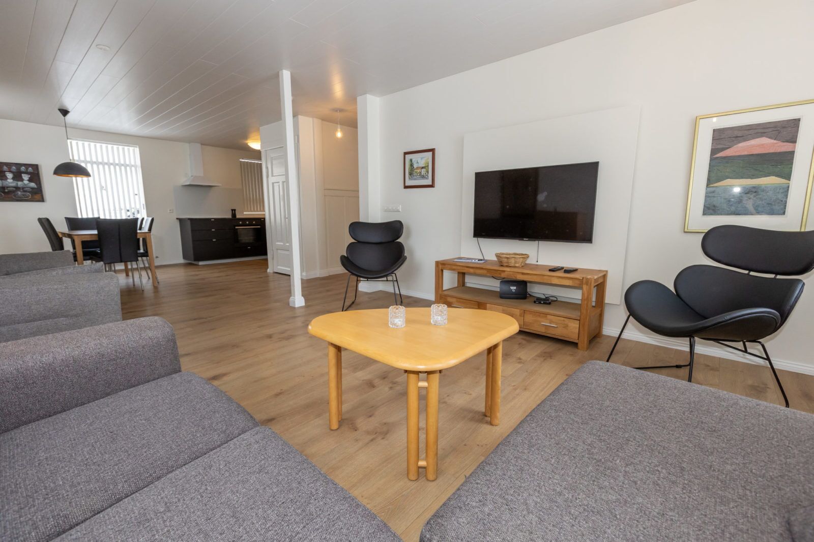 A modern living room with grey sofas, a wooden coffee table, a TV, and a dining area with a table and chairs.
