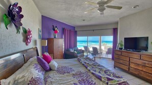 Un dormitorio con cama, televisión, ventilador de techo, vista a la playa y balcón.