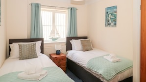 A twin room with two beds, a window with curtains, a small table with a lamp, and a painting on the wall.