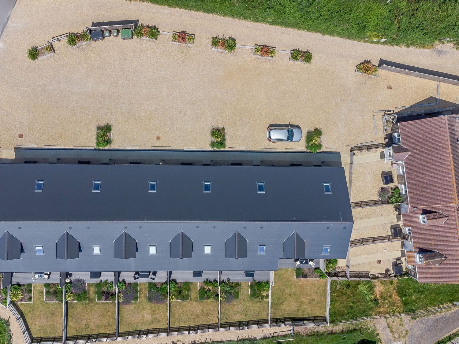 An aerial view of a building with a flat roof, multiple windows, and a parking area with a car.