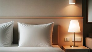 Un lit bien fait, avec du linge de lit blanc et une couverture rouge, une lampe de chevet et une table de chevet dotée d’un tiroir.