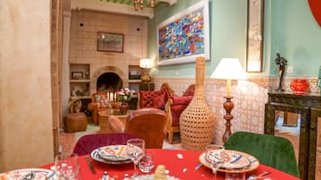 A dining area with a red tablecloth, traditional plates, and a fireplace in the background.