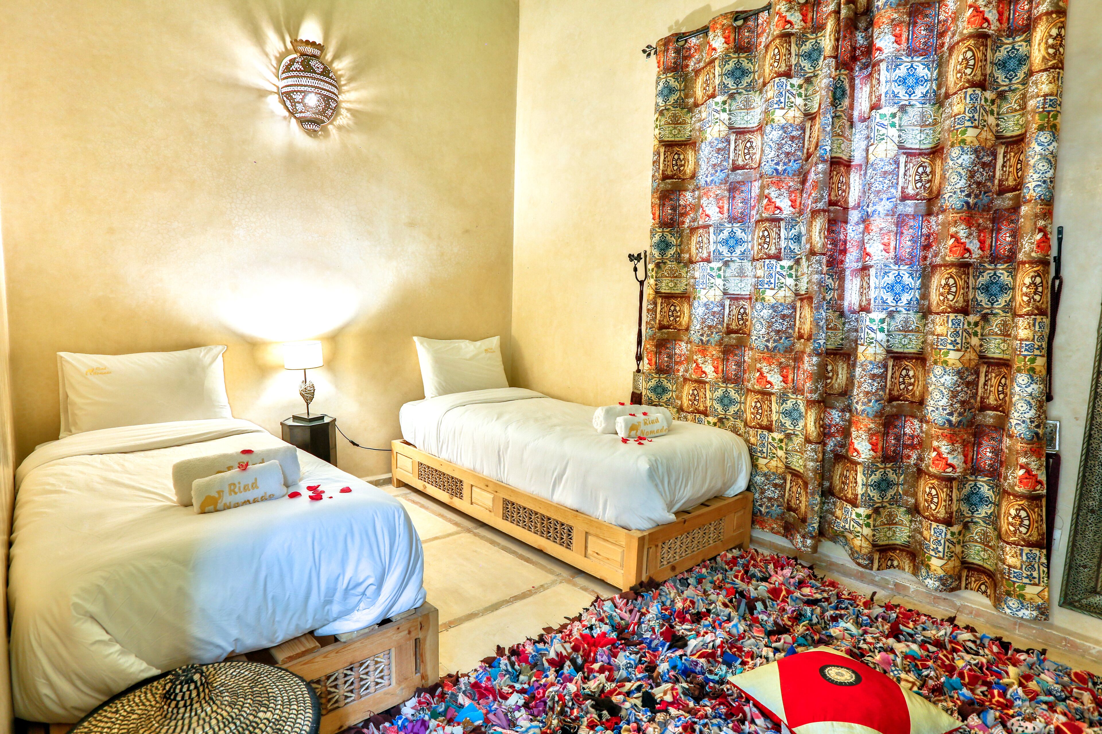Habitación de hotel con dos camas, una cortina estampada y una alfombra con objetos coloridos.