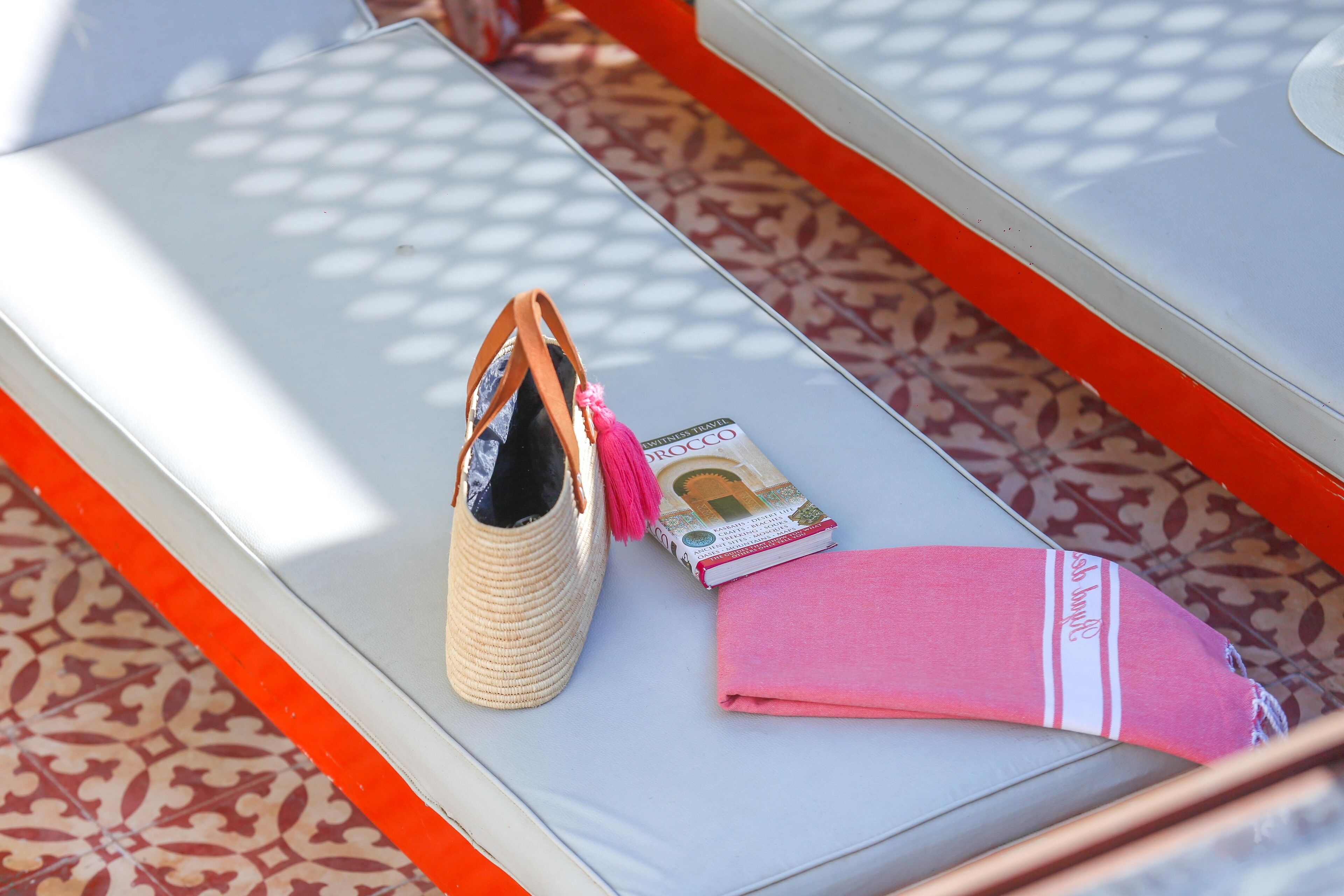 Une chaise longue avec un sac en tissu tressé et une serviette rose.