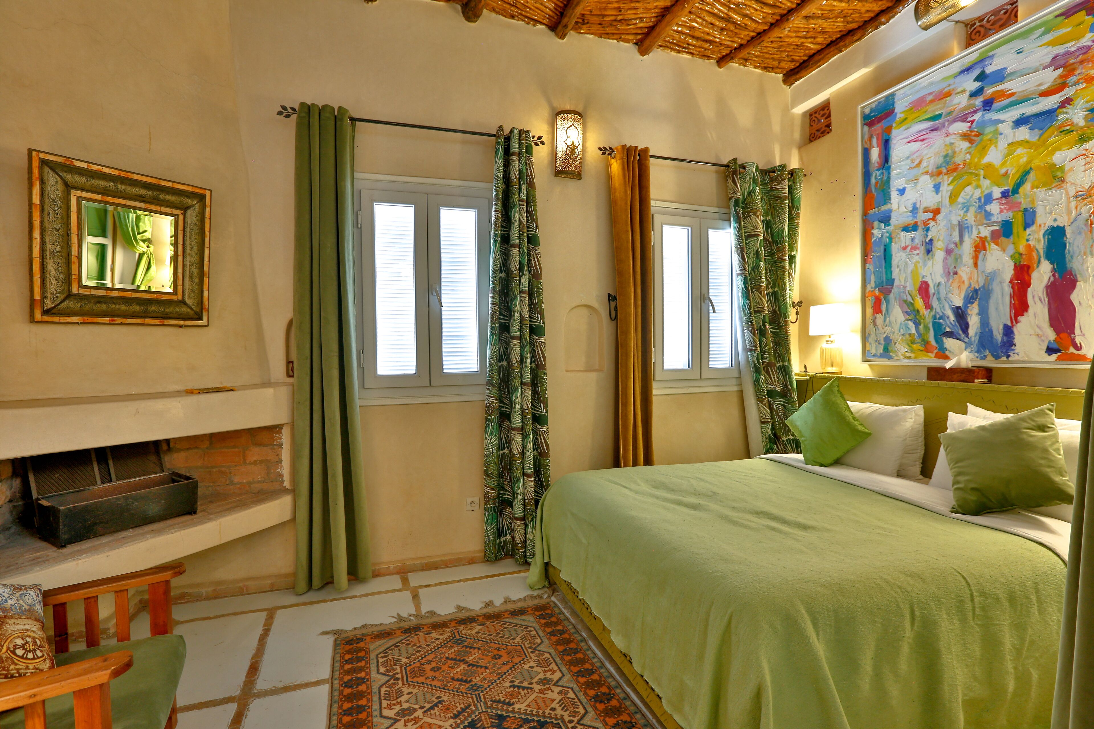 A bedroom with a bed, a fireplace, a window with curtains, and a colorful abstract painting on the wall.