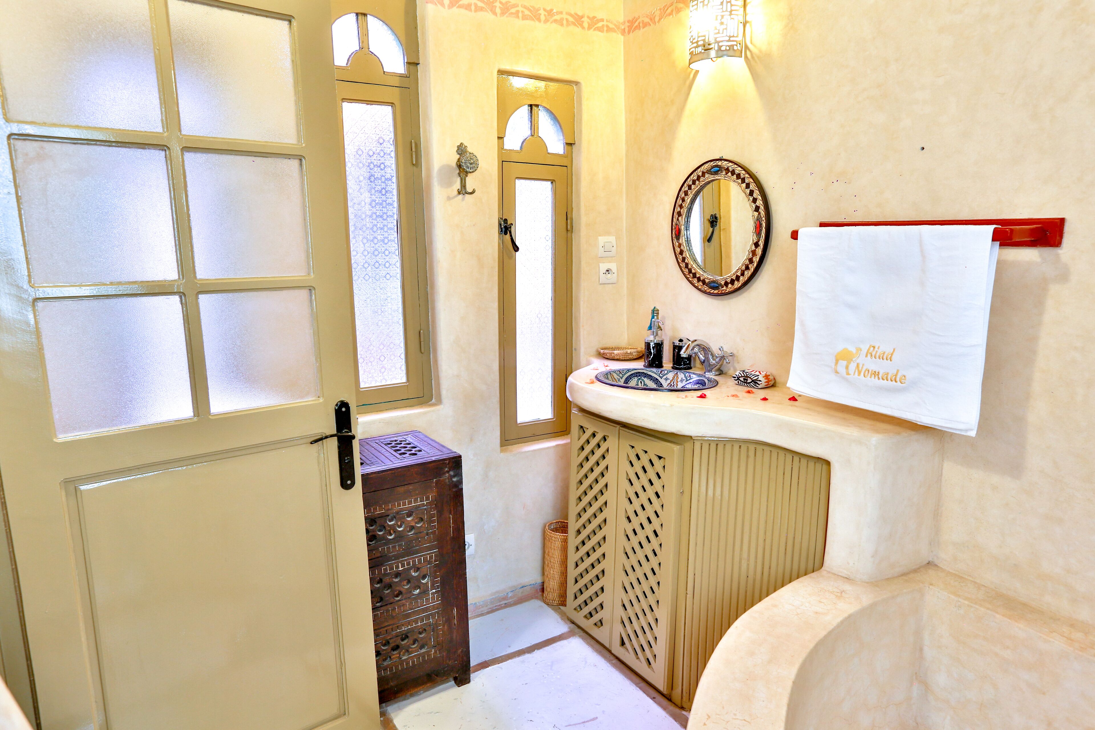 A bathroom with a bathtub, a sink with a mirror, a towel rack, and a door with frosted glass panels.