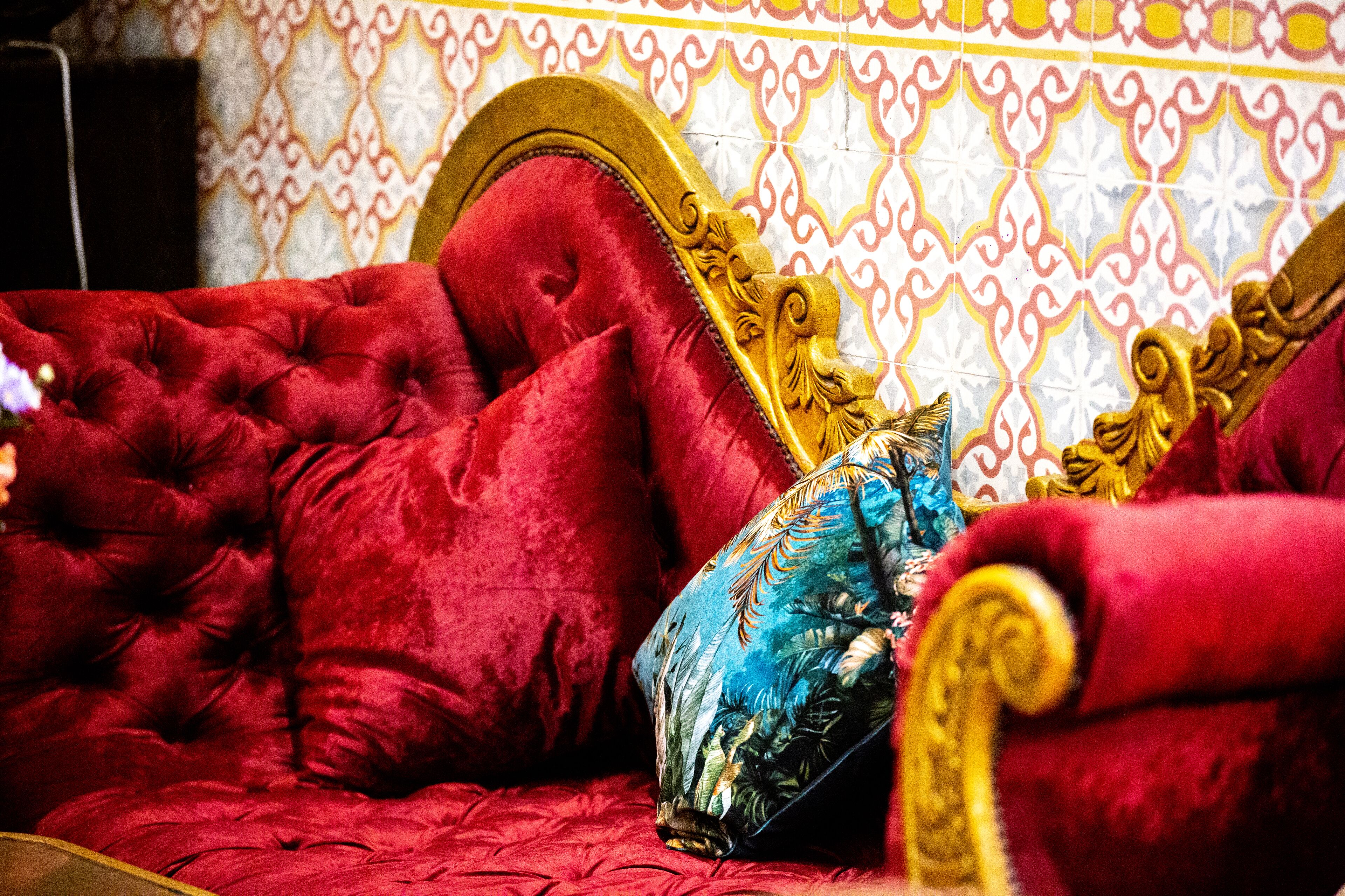 A red upholstered bed with a gold headboard and ornate detailing, set against a patterned wall.