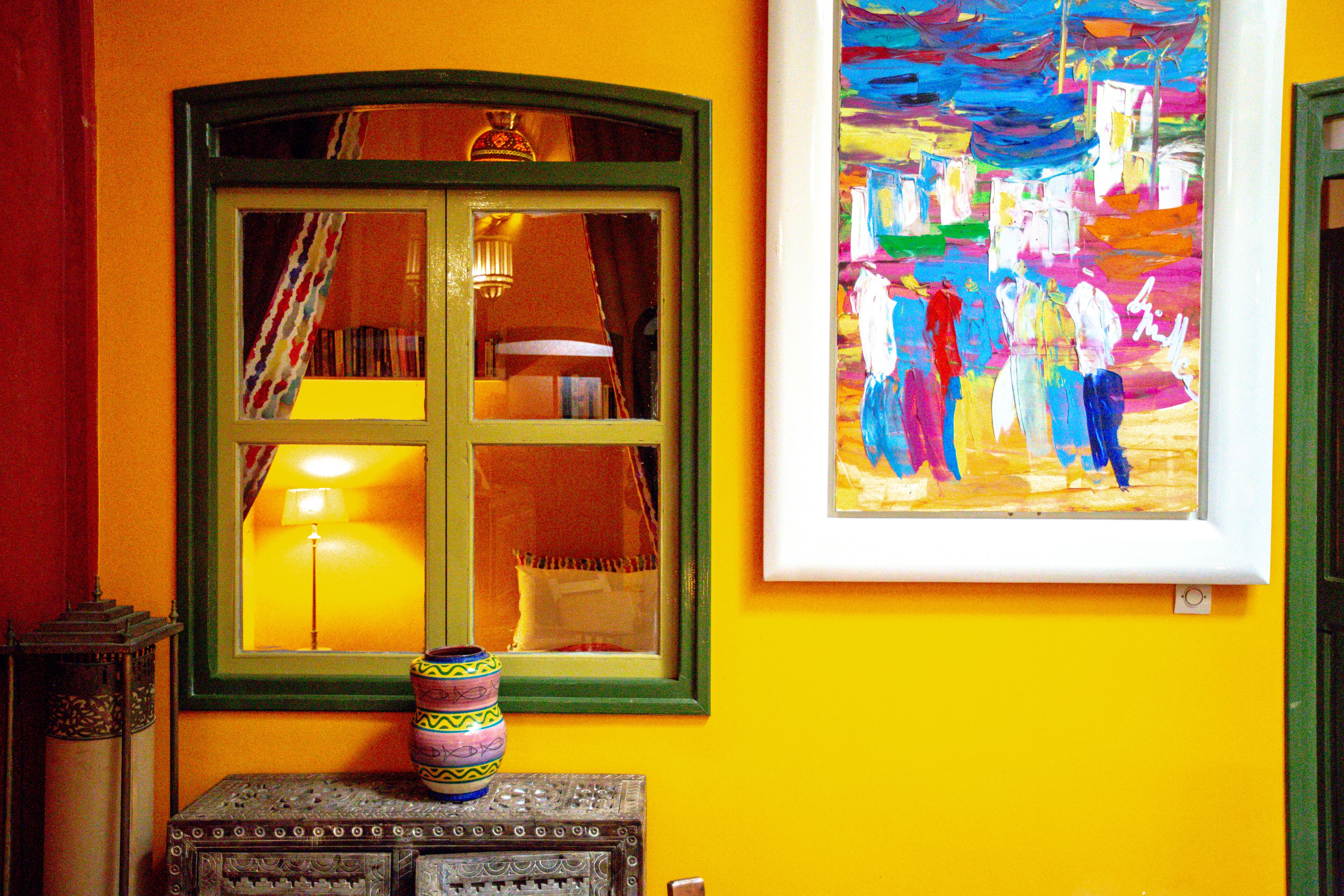 A room with a large window, a framed painting, and a decorative vase on a table.