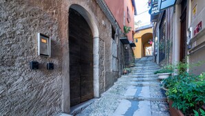 Uma estreita viela de calçada com uma grande porta em arco, paredes de pedra e uma pequena placa.