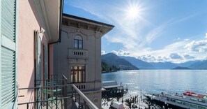 A building with a balcony overlooking a lake, a boat docked nearby, and mountains in the background. - Lakefront Retreat - Salvia (Bellagio)