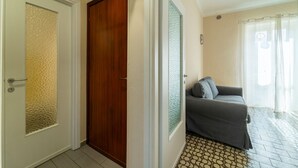 A hallway with a wooden door, a glass door with a textured pattern, and a grey sofa in a room with patterned flooring. - Lotus Apartment With Lakeview (Bellagio)