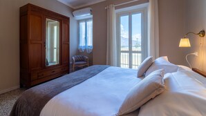 A hotel room with a large bed, a wooden wardrobe, a chair, and a balcony with a view. - Lotus Apartment With Lakeview (Bellagio)