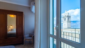 A room with a wooden wardrobe, a chair, and a view of a clock tower through a window. - Lotus Apartment With Lakeview (Bellagio)