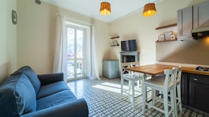 A compact living space with a sofa, dining table, chairs, a TV, and a kitchenette. - Lotus Apartment With Lakeview (Bellagio)