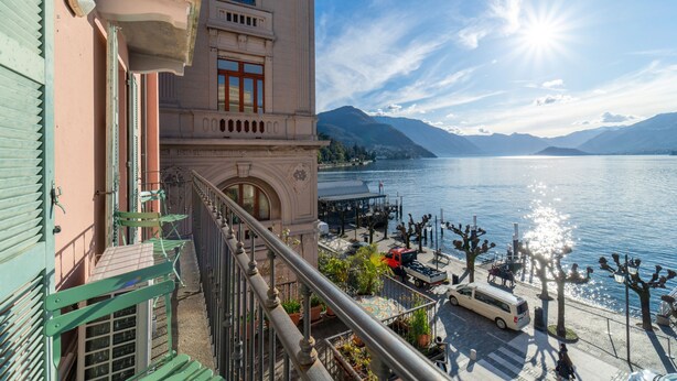 Ein Gebäude mit einem Balkon, der auf einen See und Berge im Hintergrund blickt, sowie einem Steg.