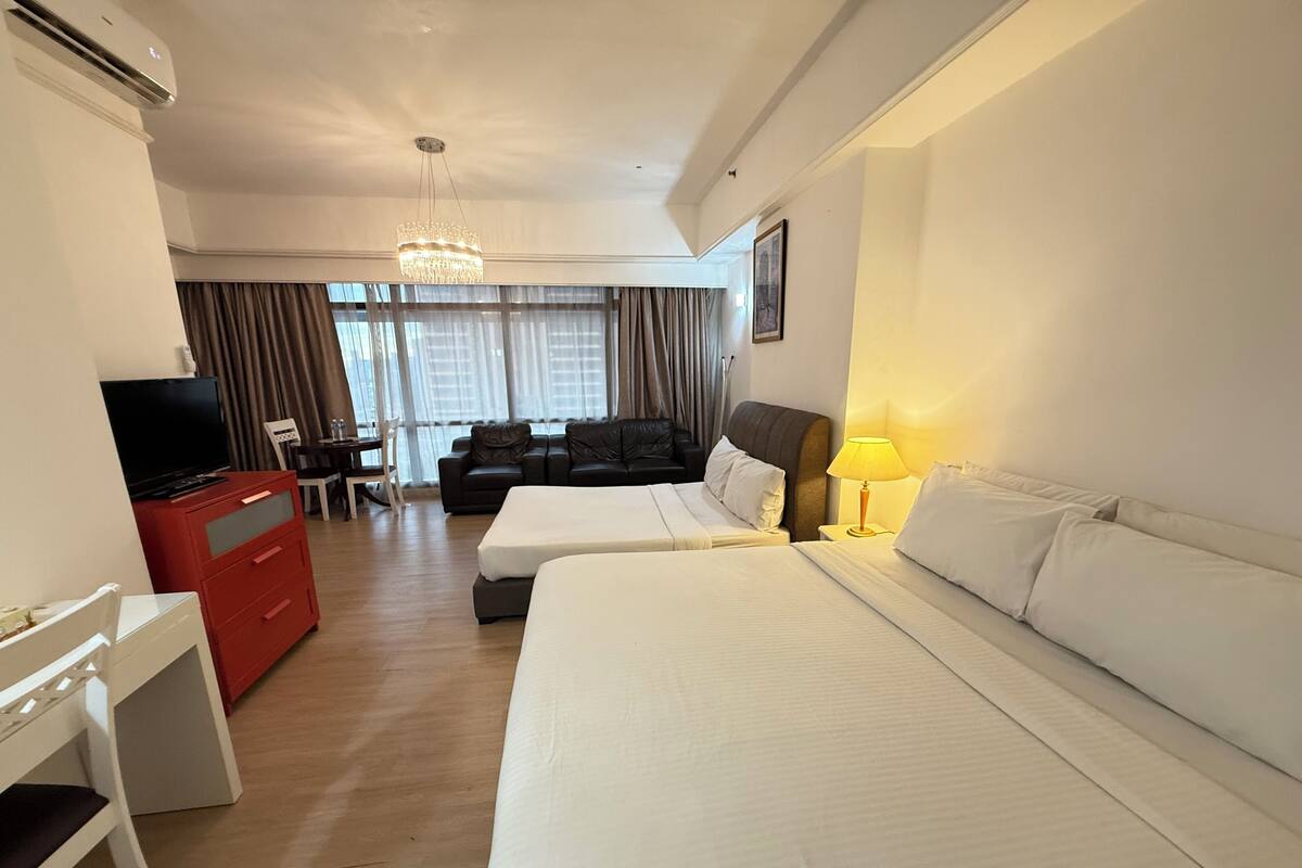 A hotel room with a large bed, a desk with a TV, a sofa, and a chandelier.