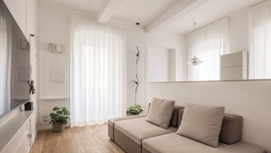 Una sala moderna con un sofá color beige, un televisor de pantalla plana y piso de madera.