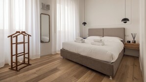 Un dormitorio con una cama, un perchero de madera, un espejo y una mesita de noche con una lámpara.