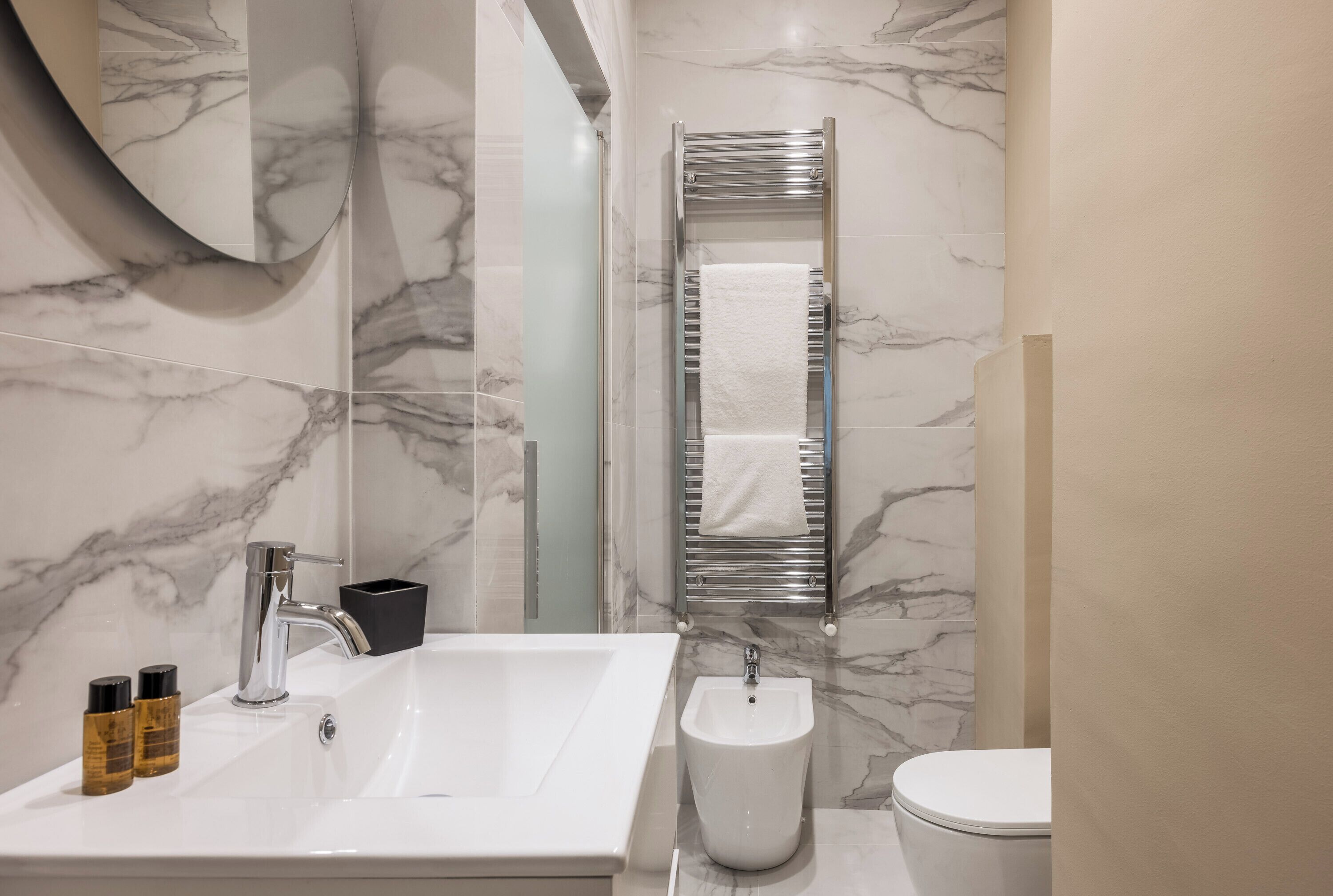 A modern bathroom with a marble backsplash, a white sink, a bidet, and a towel rack.