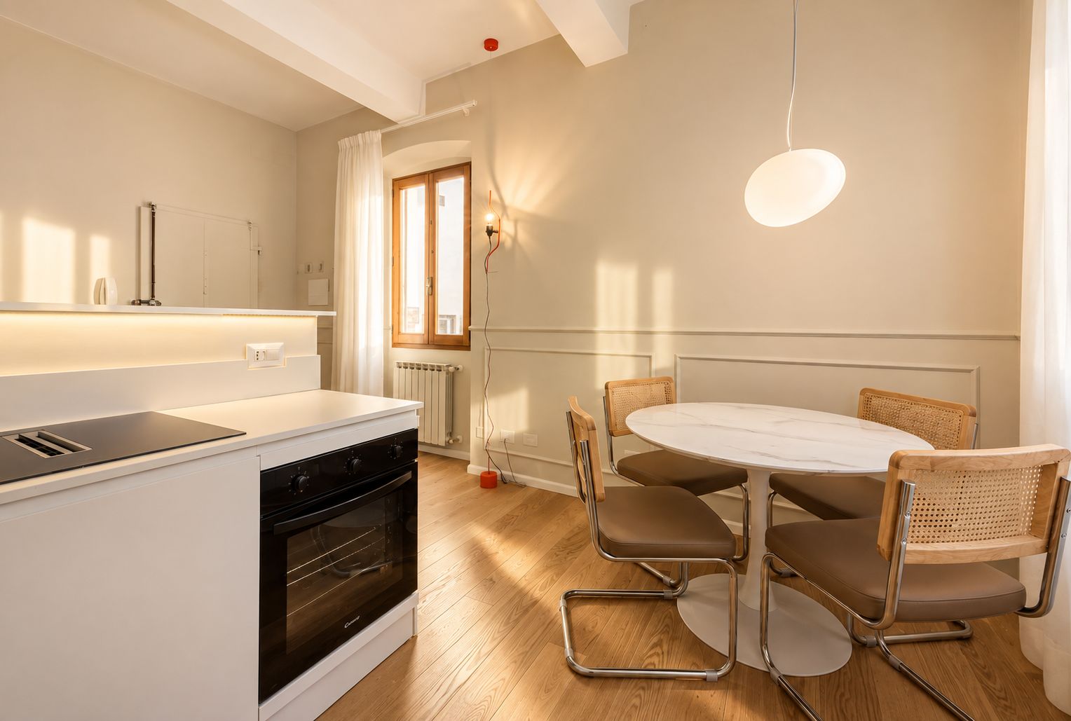 A modern kitchen with a white countertop, a built-in oven, and a dining area with a round table and four chairs.