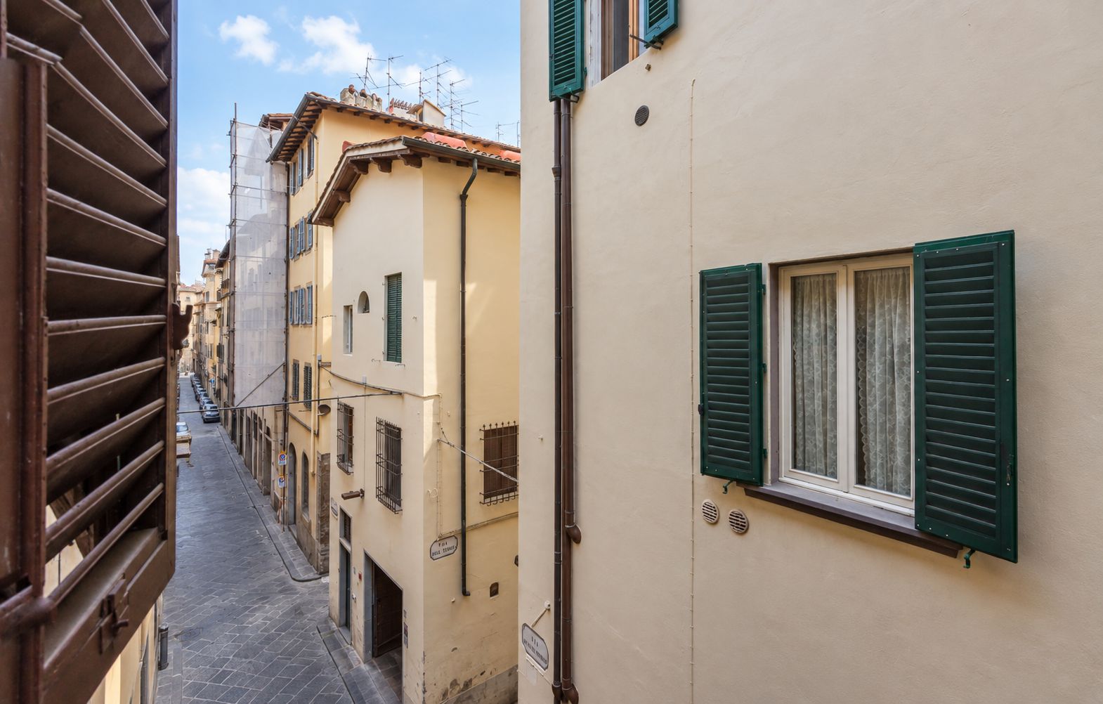 A narrow street with buildings on either side, featuring traditional architecture with shutters and a cobblestone path.