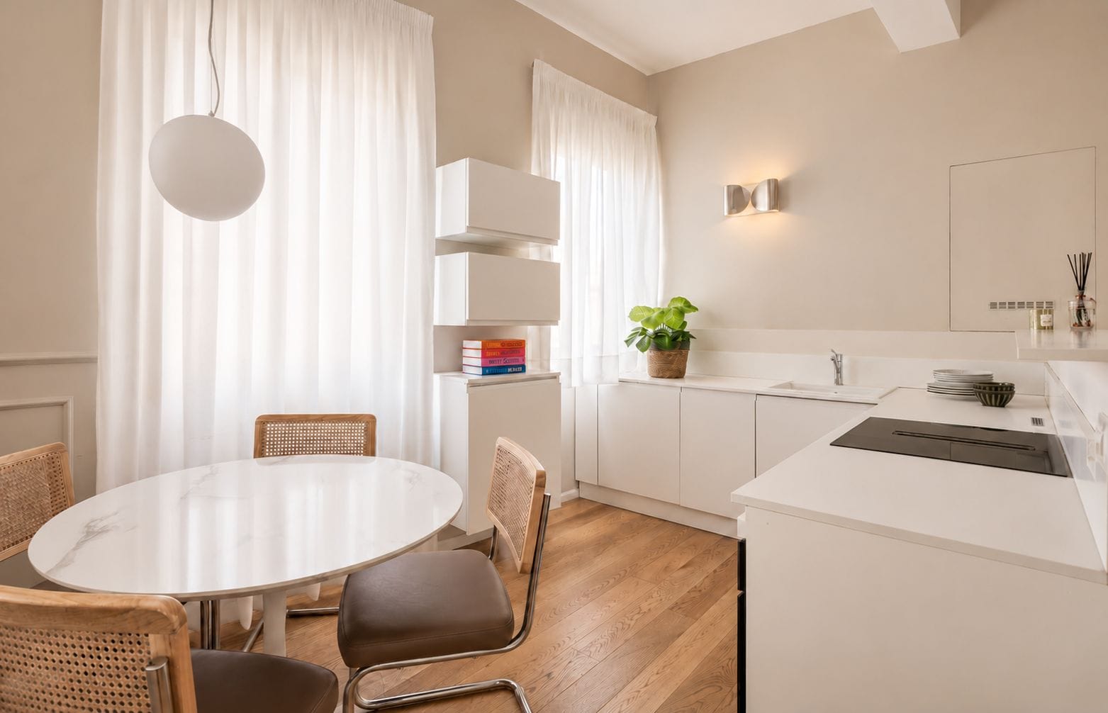 A modern kitchen with white cabinetry, a round dining table, and a hanging light fixture.