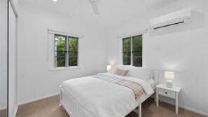 A bedroom with a bed, two bedside tables, a ceiling fan, and an air conditioning unit. - West End Gem Near Attractions (West End)