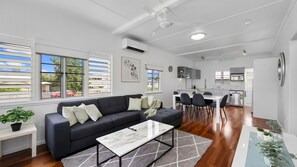 A modern living space with a dark sofa, a white coffee table, and a dining area with chairs. - West End Gem Near Attractions (West End)