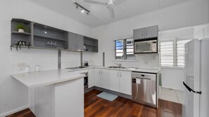 A modern kitchen with white cabinetry, a built-in microwave, and a stainless steel dishwasher. - West End Gem Near Attractions (West End)