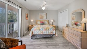 Ein Schlafzimmer mit Bett, Nachttischen, Kommode, Deckenventilator und großem Fenster.