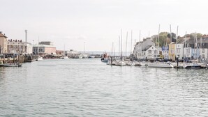 A marina with boats docked along the waterfront, buildings on the shore, and a clear sky. - Emminster (Weymouth)