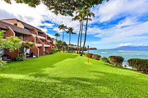 Um hotel com um gramado bem cuidado, palmeiras e vista para o oceano.