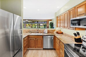 A modern kitchen with stainless steel appliances, wooden cabinets, and a large window overlooking a garden.
