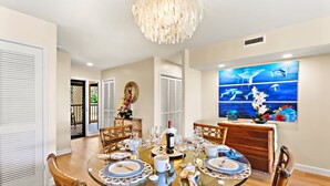A dining room with a round glass table set for six, surrounded by wooden chairs.