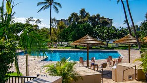 A swimming pool with lounge chairs and umbrellas, surrounded by palm trees and greenery.