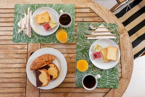 A wooden table with breakfast items including toast, croissants, and juice, set on a green leaf-patterned placemat. - Vasia s House in Kalivia (Saronikos)
