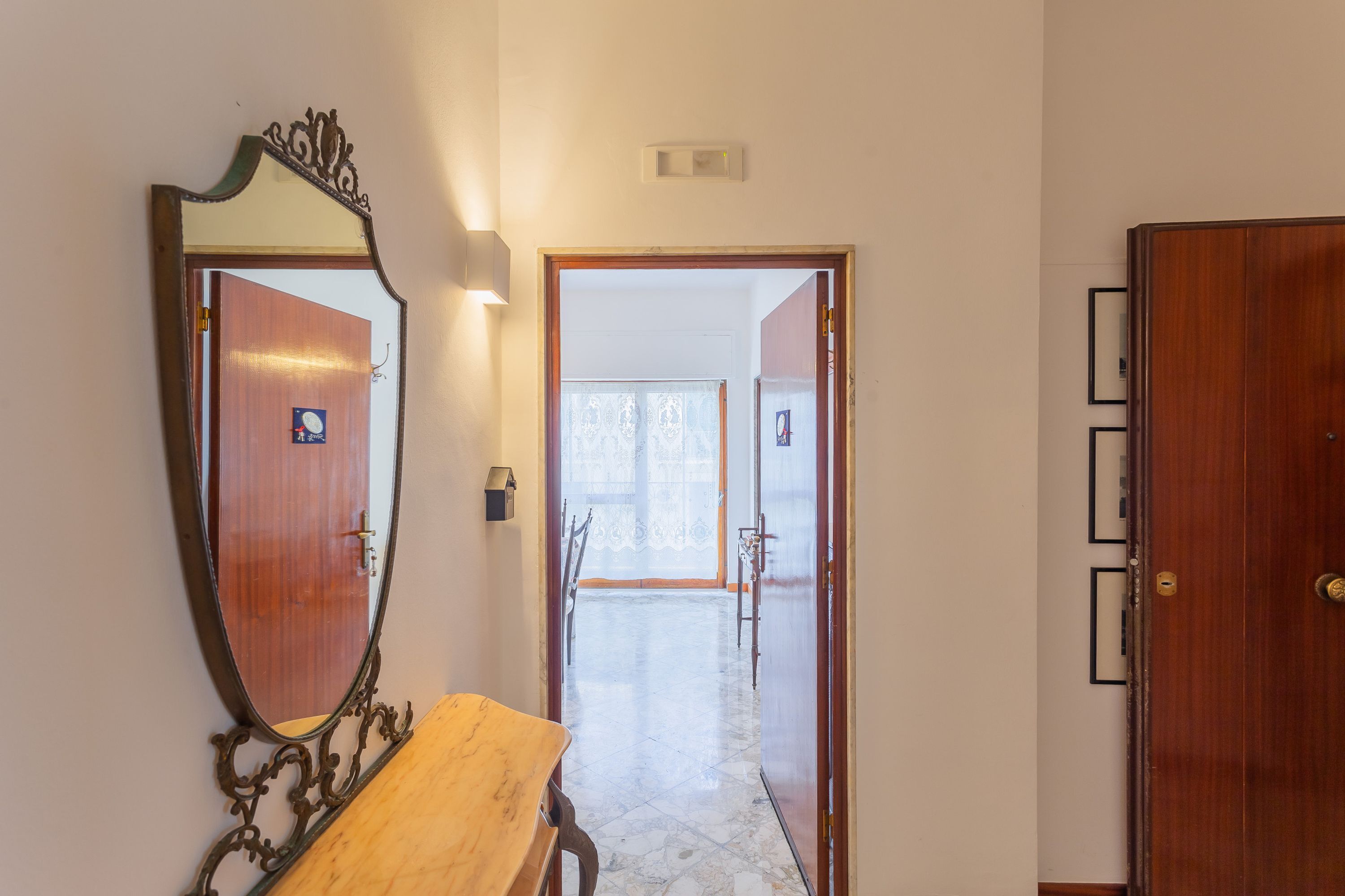 A hallway with a wooden bench, a large mirror, and a door leading to a room.