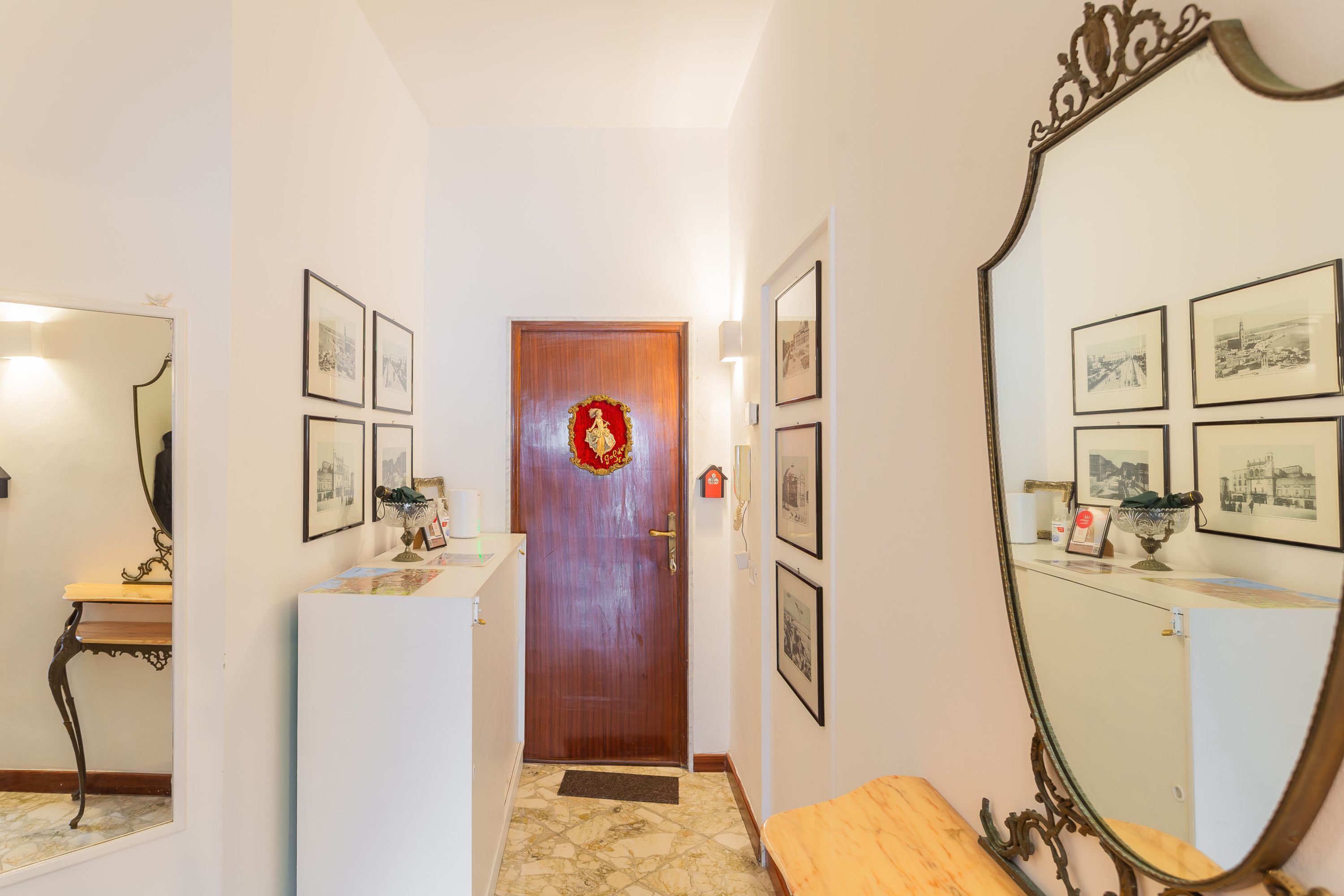 Un couloir avec une porte en bois, des tableaux encadrés accrochés aux murs, un miroir et un banc.
