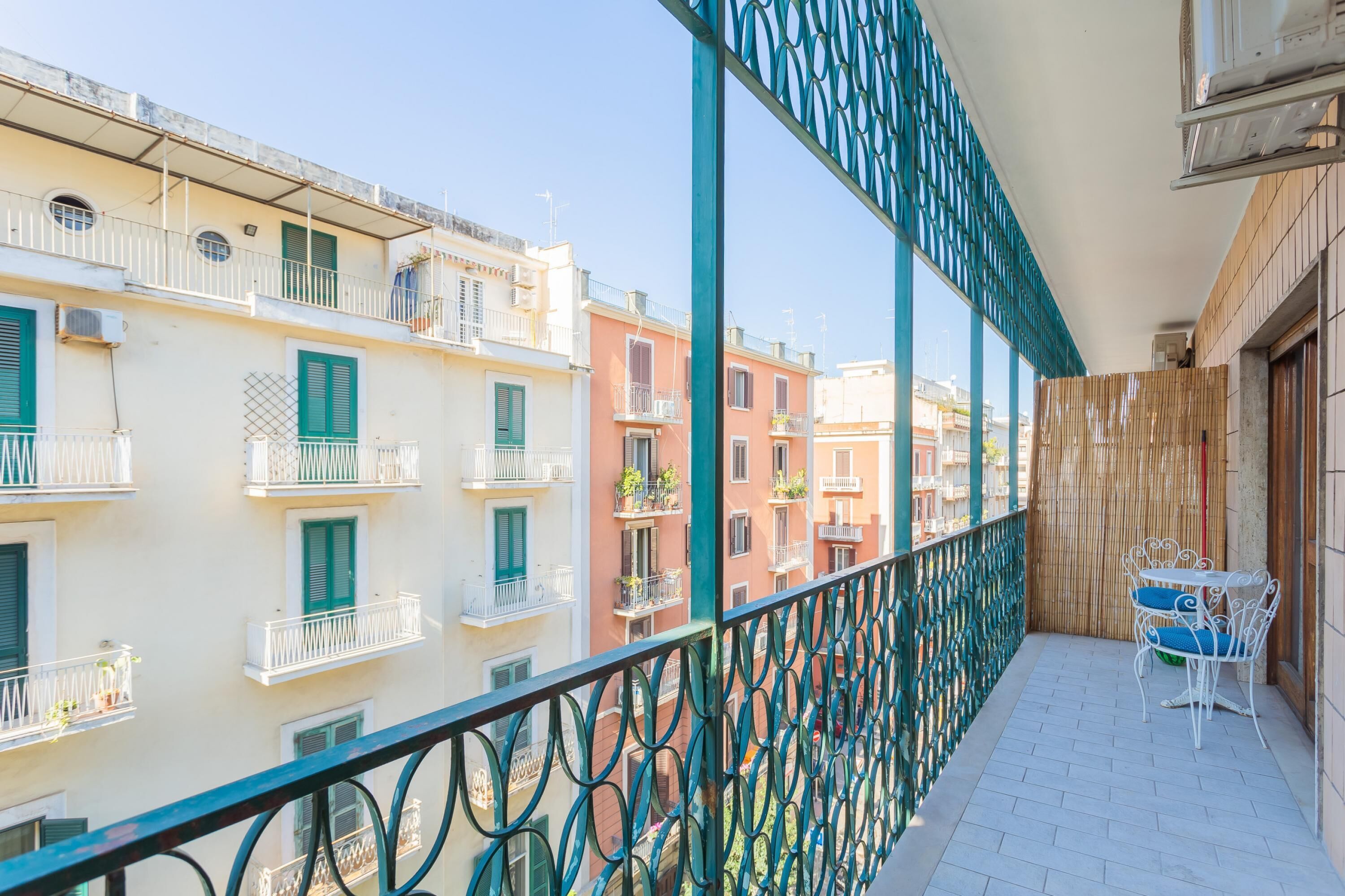 A balcony with a view of colorful buildings, a metal railing, and a small table with chairs.