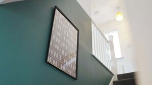 Een lijst met een foto aan een groenblauwe muur, een trap en een lamp.