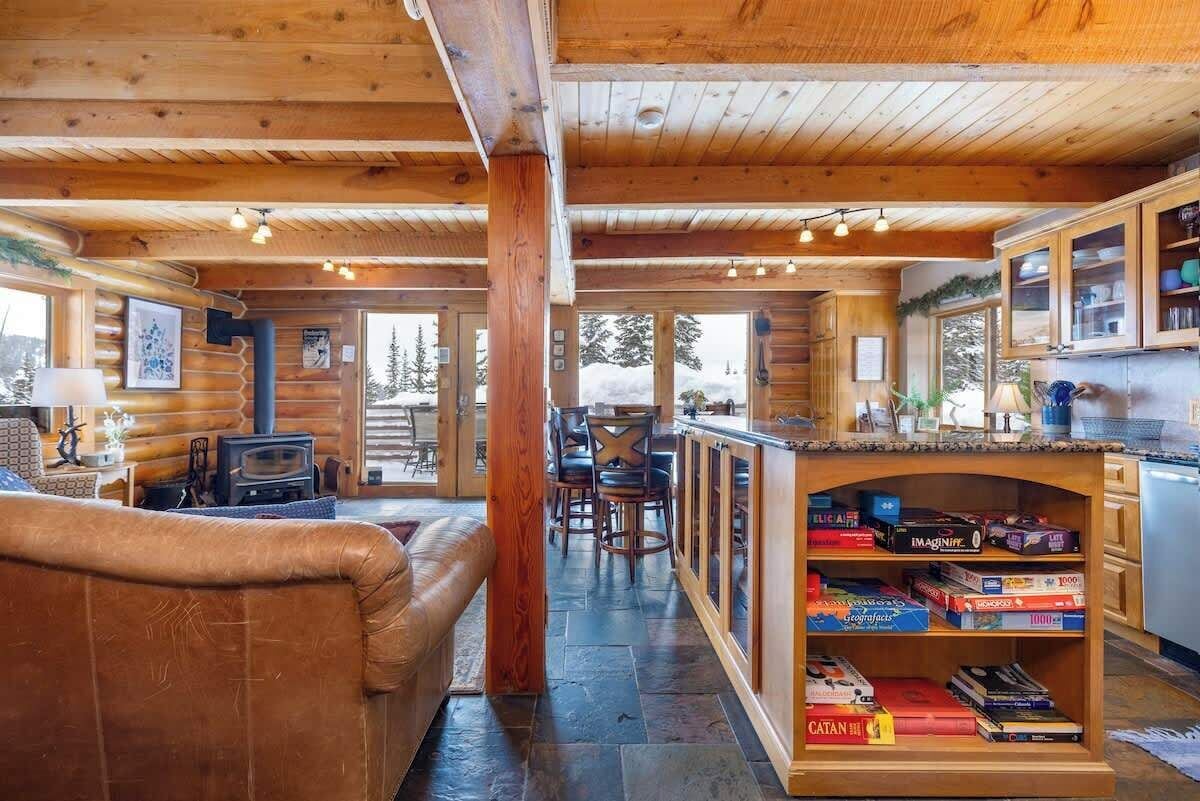 Een gezellig chaletinterieur met houten inrichting, een open haard, een barhoek met gezelschapsspellen en een eethoek met stoelen en een tafel.