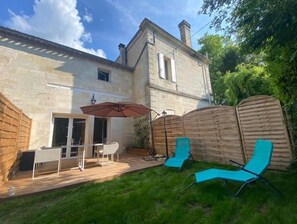 Une maison en pierre avec un patio, une table et des chaises, ainsi que deux fauteuils bleus.