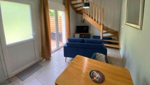 A living room with a wooden staircase, a blue sofa, a wooden table, and a TV. - Coin de Paradis en Bord de Dordogne 2 (La Riviere)