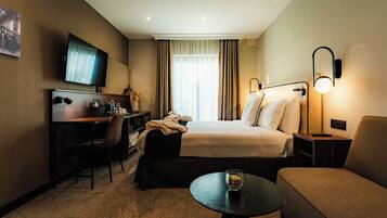 A hotel room with a bed, a desk, a chair, a table, a TV, and a lamp.