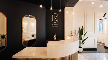 A hotel reception area with a modern design, featuring a reception desk, a large mirror, and a logo on the wall.