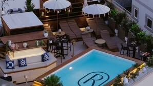 Ein Pool auf dem Dach mit einem 'R'-Logo, Sitzgelegenheiten im Freien, Sonnenschirmen und Topfpflanzen.