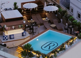A rooftop pool with a 'R' logo, outdoor seating, umbrellas, and potted plants.