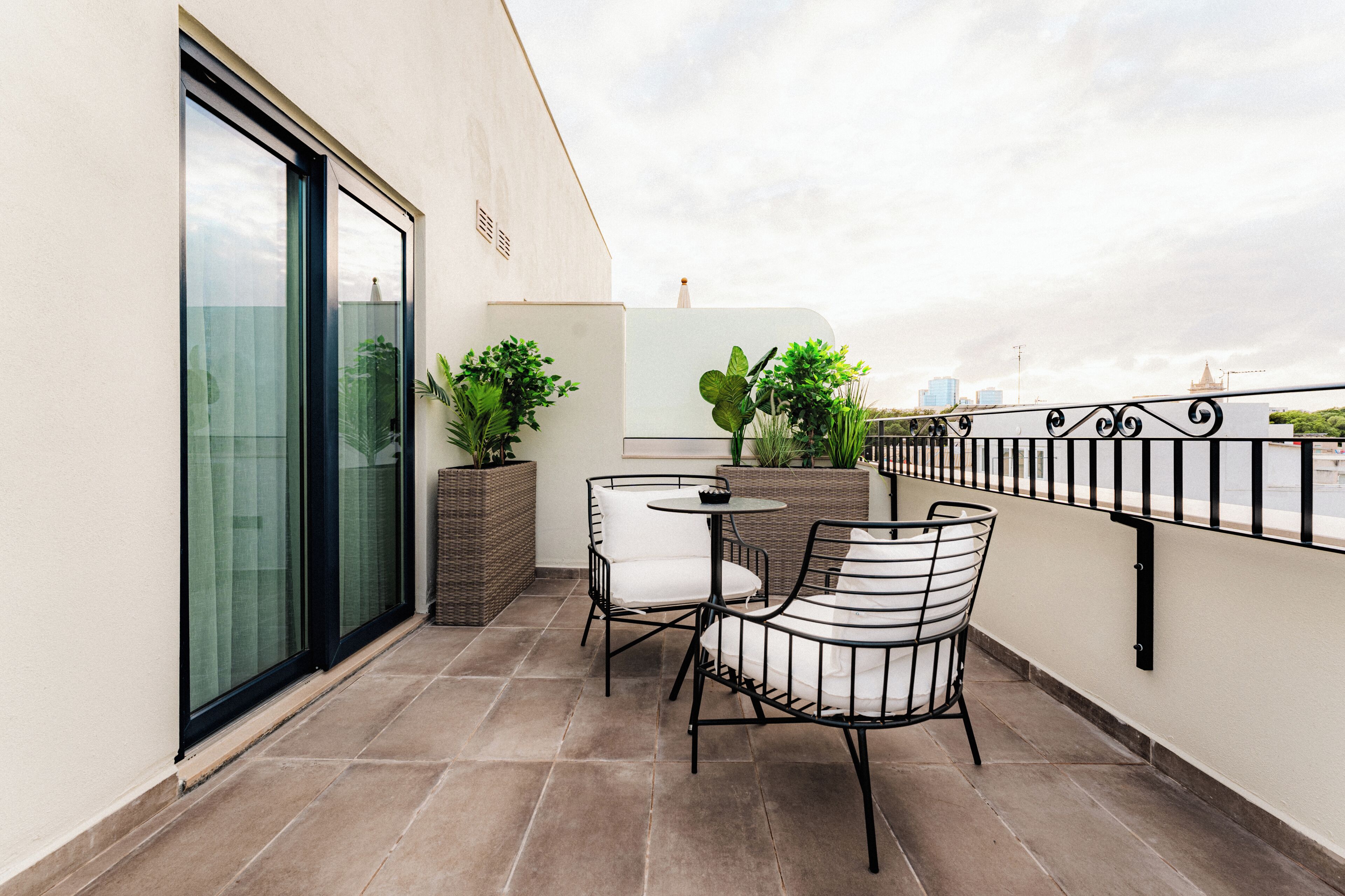 A balcony with a table and chairs, potted plants, and a view of the city skyline.